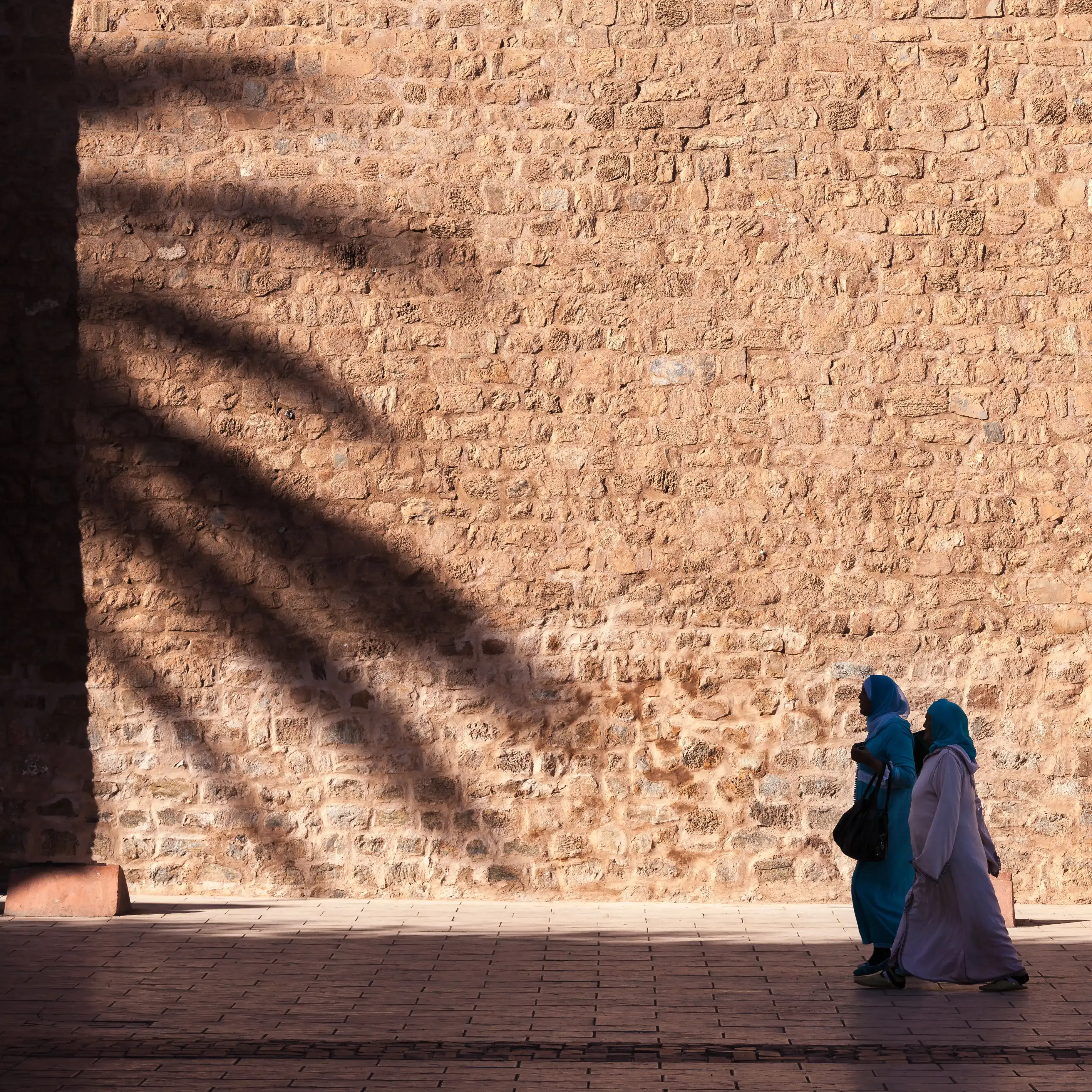 Des ombres sur un mur et des piétons à Marrakech